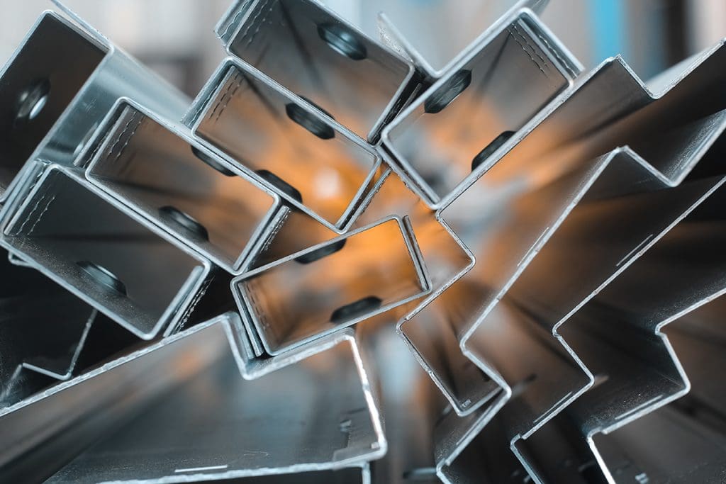 A stack of aluminum frame pieces viewed in profile, with an out-of-focus yellow object visible behind the stack.