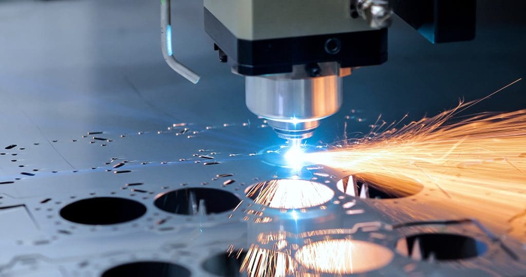 A laser-cutting machine in action, a close-up of a metal plate with holes cut through it as a laser diode is held near the plate, and sparks are sent out from the point of contact.