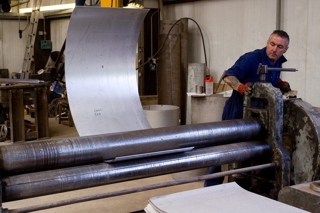 A metal fabrication worker utilizing a metal roller to shape a plate of steel.