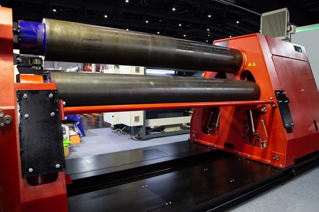 a large metal rolling machine, which consists of three long metal rollers in a triangle shape, held by two bright orange triangular boxes