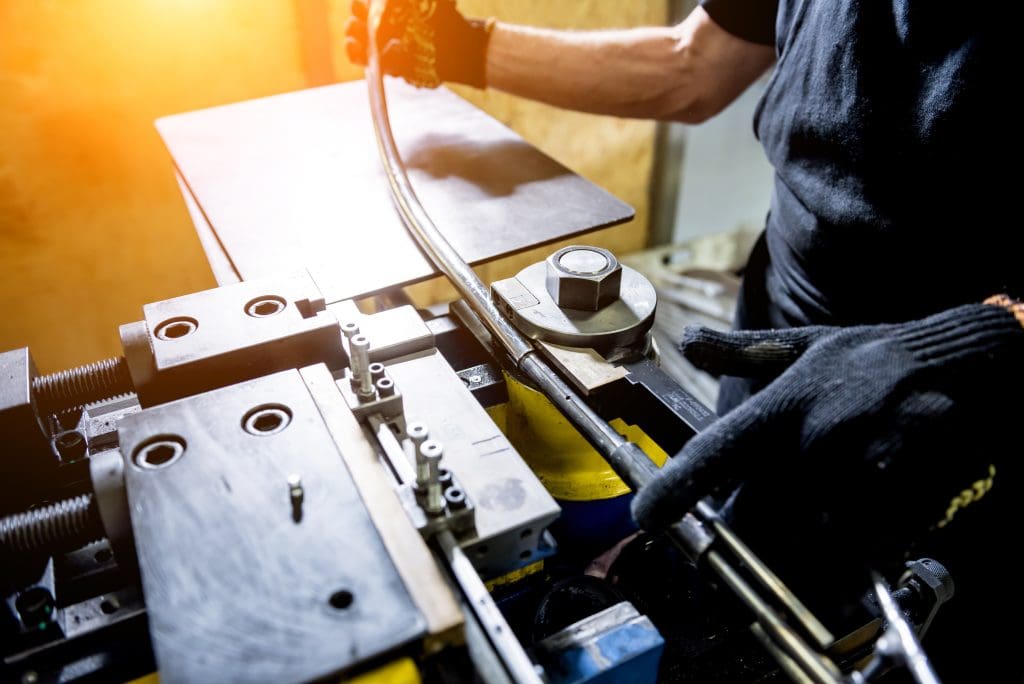 A metalworker bends a length of steel pipe using a pipe-bending machine