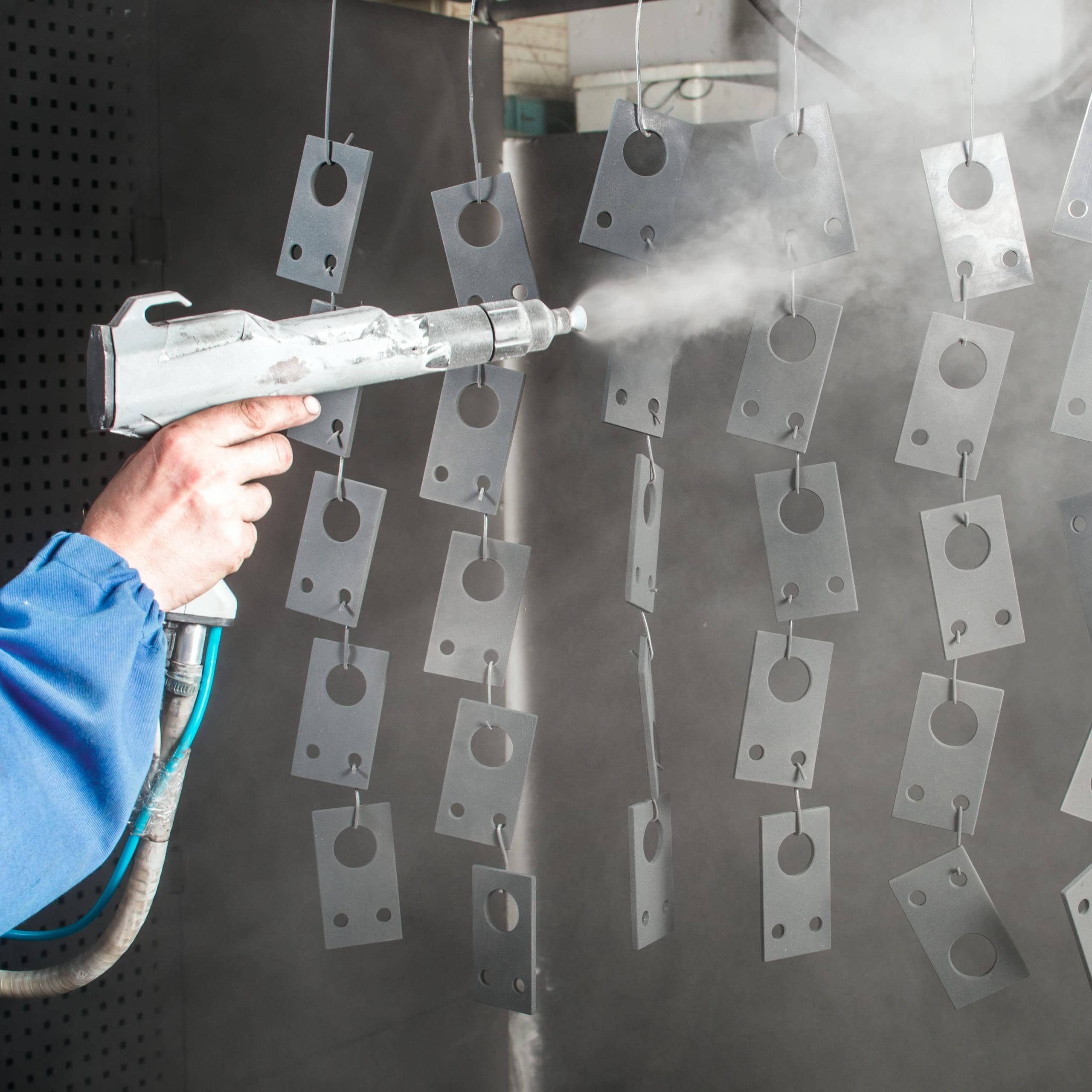 A number of small metal parts hanging from hooks as they are sprayed with a silver powder coating