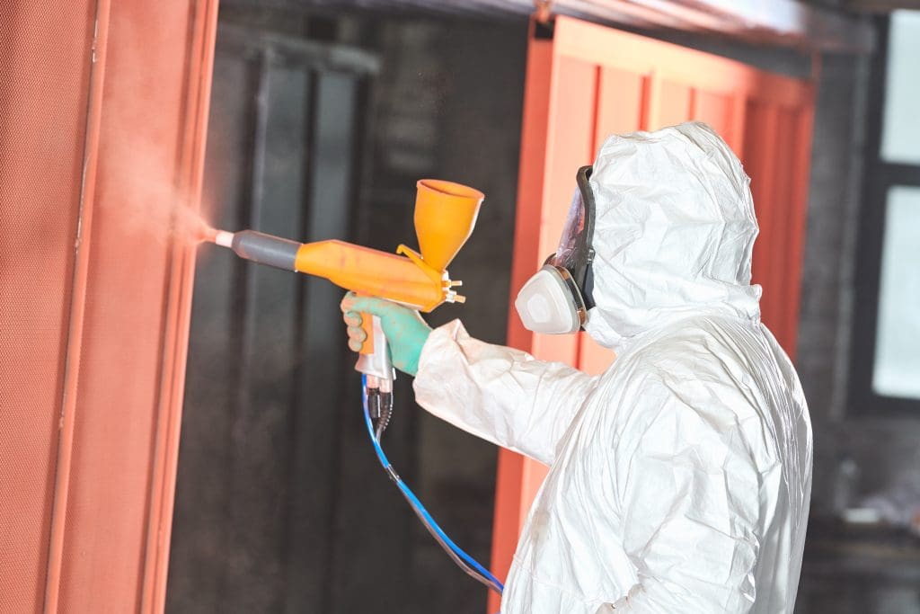 A powder-coating specialist applies an orange coating to a large metal door in production