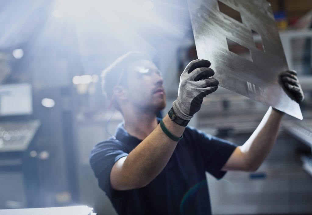 A metal fabricator examining a piece of metal with rectangular parts removed.