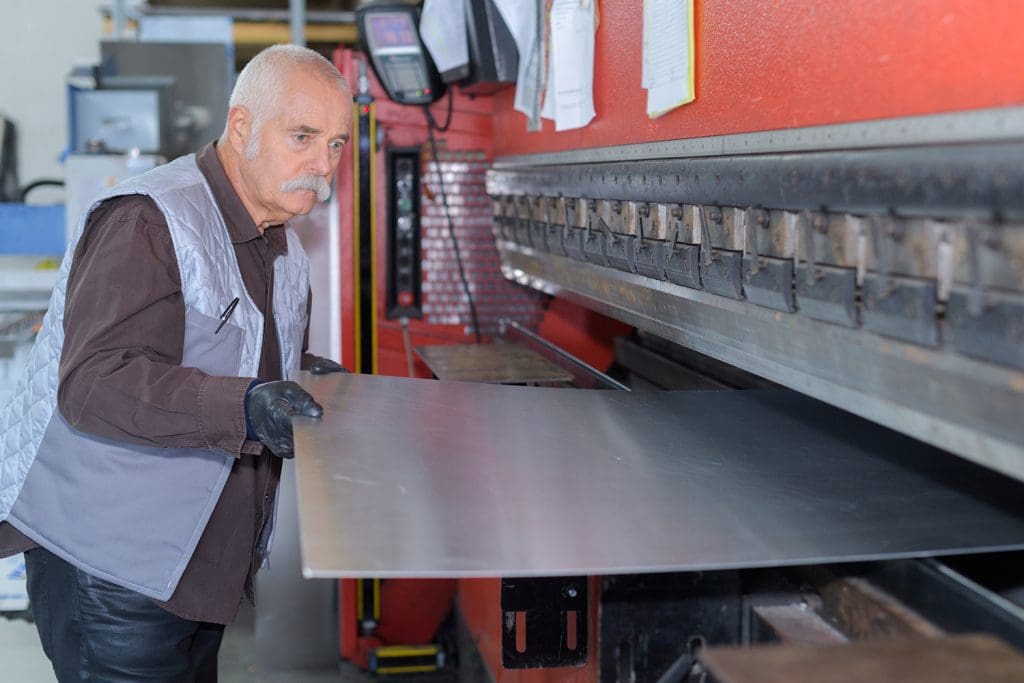 a metalworker using a large cutting machine to shear a piece of sheet metal